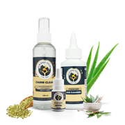 The "Fur Ball Story" hygiene family gathered together: Canni Clean mouth spray, Clear Ear cleanser, and Blink Ease eye drops. They are flanked by raw ingredients like fennel seeds and towering aloe vera leaves, representing a complete natural wellness toolkit for pets.